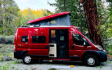 A red Winnebago Solis camper van, an ideal RV rental, parked in a scenic forest with its pop-top extended.