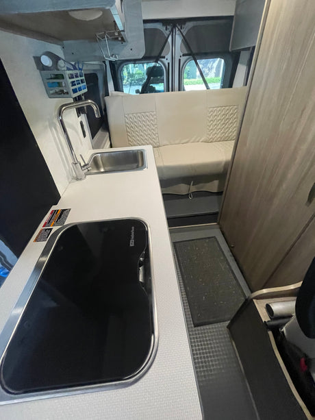 RV rental interior: Kitchen with sink, Suburban cooktop, overhead storage, and textured bench seating.