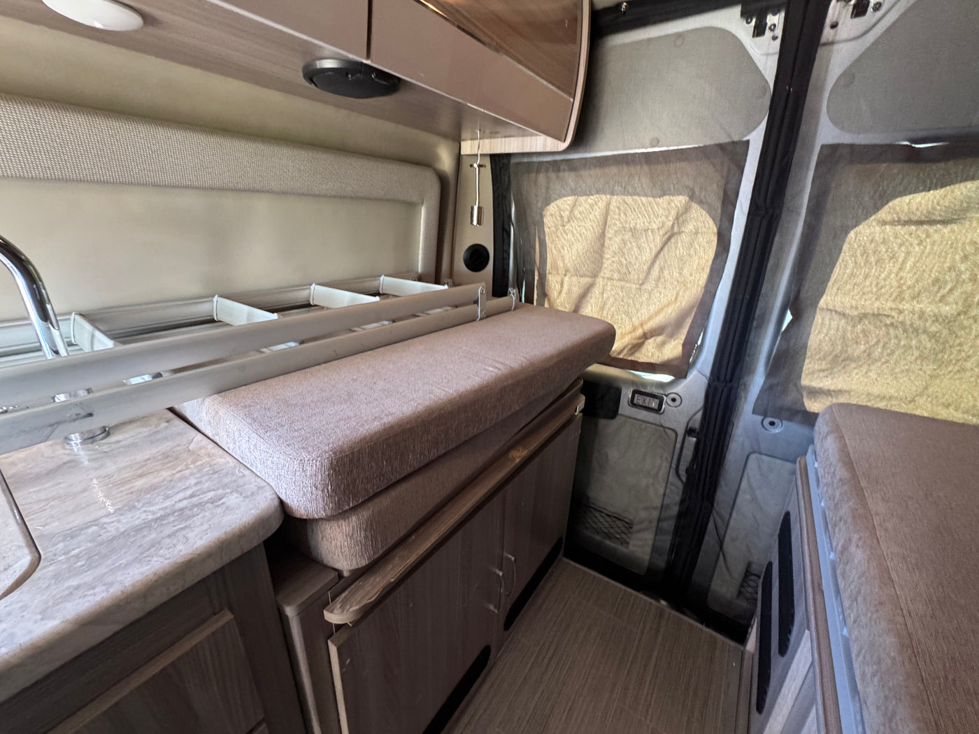 Interior of an RV rental showing a compact kitchenette with sink, cushioned seating, cabinetry, and window shades. — photo 9