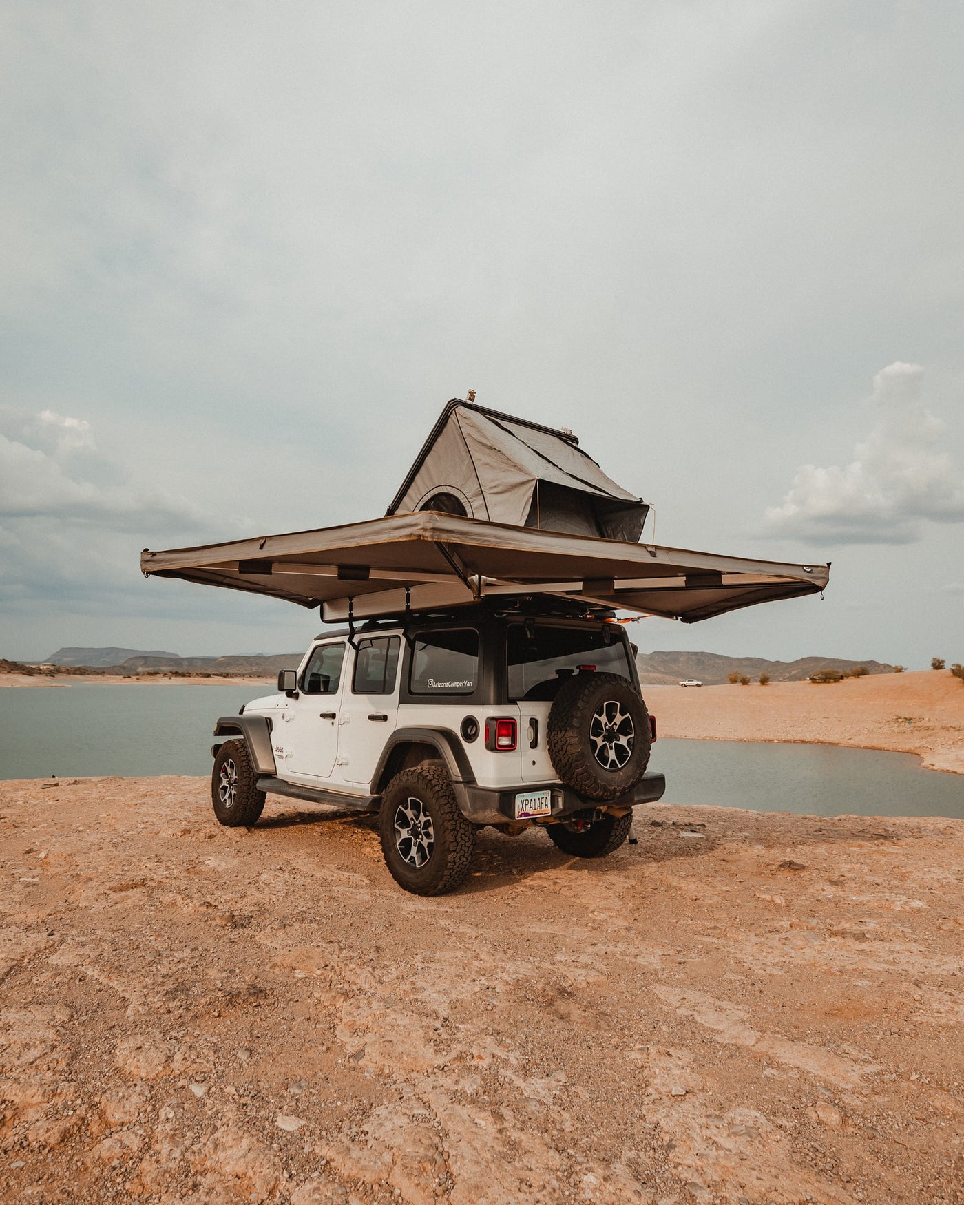 White Jeep Wrangler with rooftop tent & awning by a lake, ideal for an RV rental outdoor escape. — photo 8
