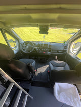 Inside an RV rental: front cabin with dashboard, seats, and a ladder, looking out to a green field.