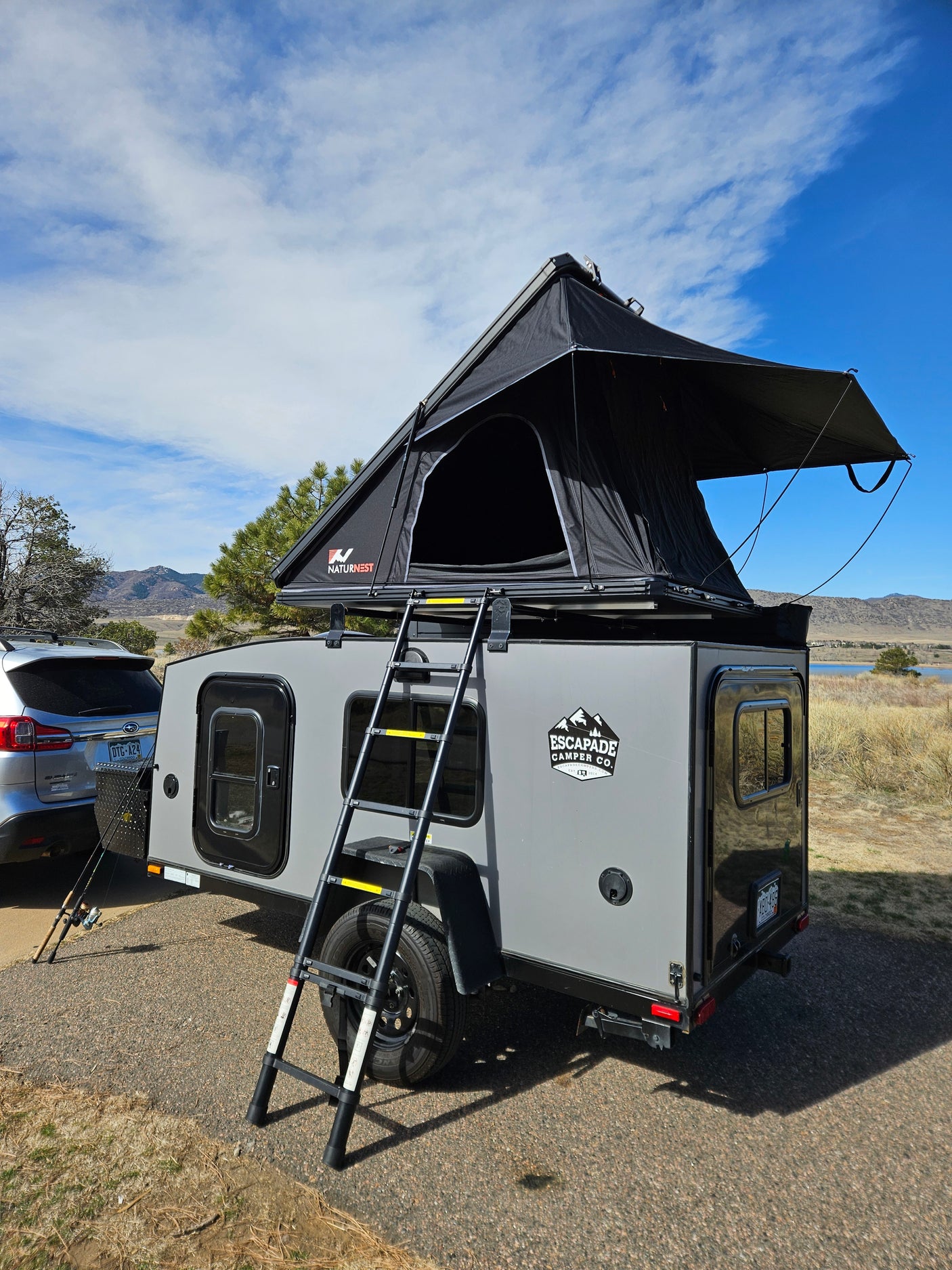 Explore the outdoors! A grey teardrop camper trailer with a rooftop tent is hitched to an SUV, ready for your RV rental camping trip.