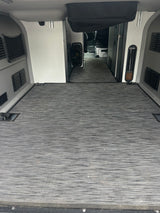 RV rental interior: Spacious cargo/living area with gray textured flooring, side panels, vents, and tie-downs, leading to the cab.