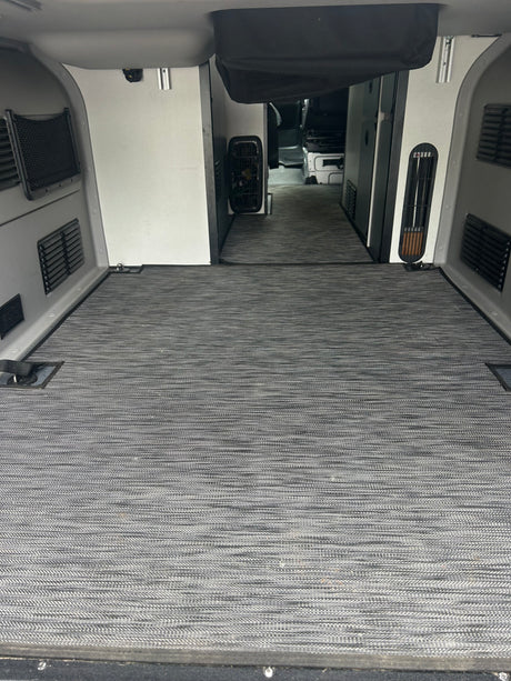 RV rental interior: Spacious cargo/living area with gray textured flooring, side panels, vents, and tie-downs, leading to the cab.