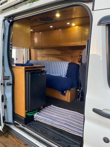 RV rental: Step inside this custom camper van, featuring a mini-fridge, wooden cabinets, and a bed.