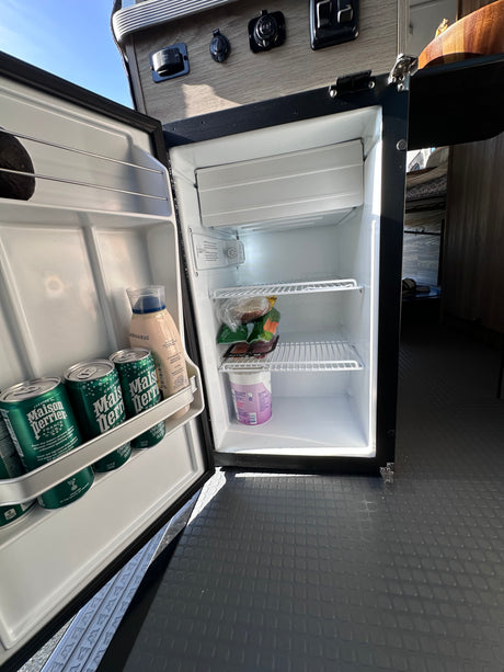 Compact mini-fridge in an RV rental, stocked with drinks and snacks for your adventure. Ideal for travel needs.