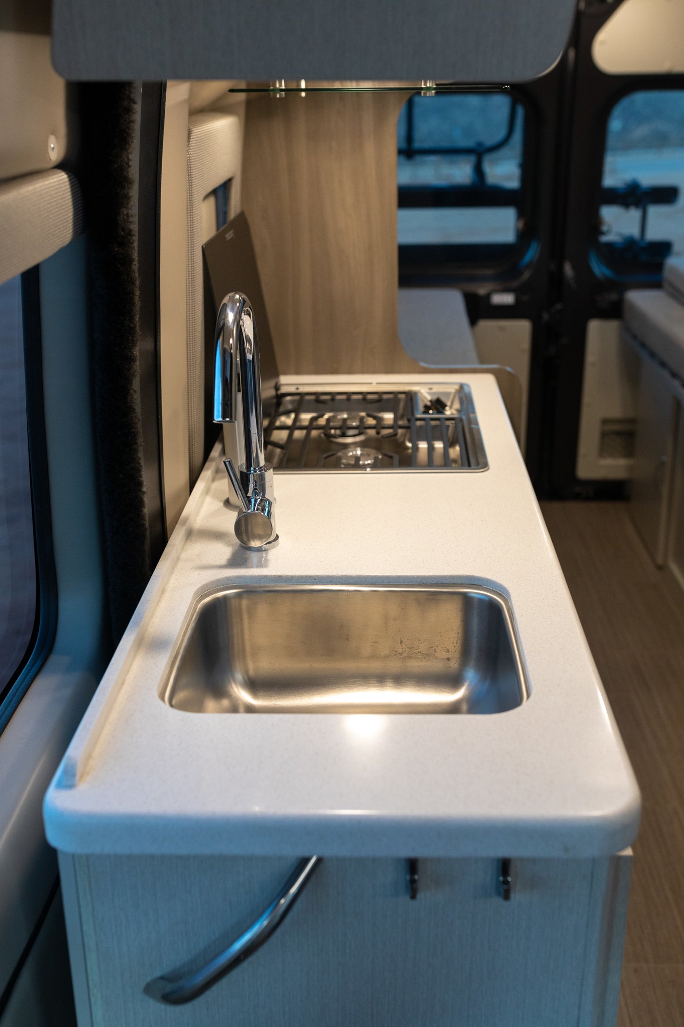 RV rental interior: A bright, compact kitchen features a stainless steel sink, shiny chrome faucet, and built-in two-burner stovetop.