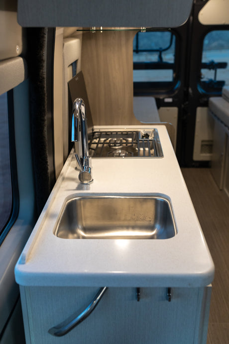 RV rental interior: A bright, compact kitchen features a stainless steel sink, shiny chrome faucet, and built-in two-burner stovetop.