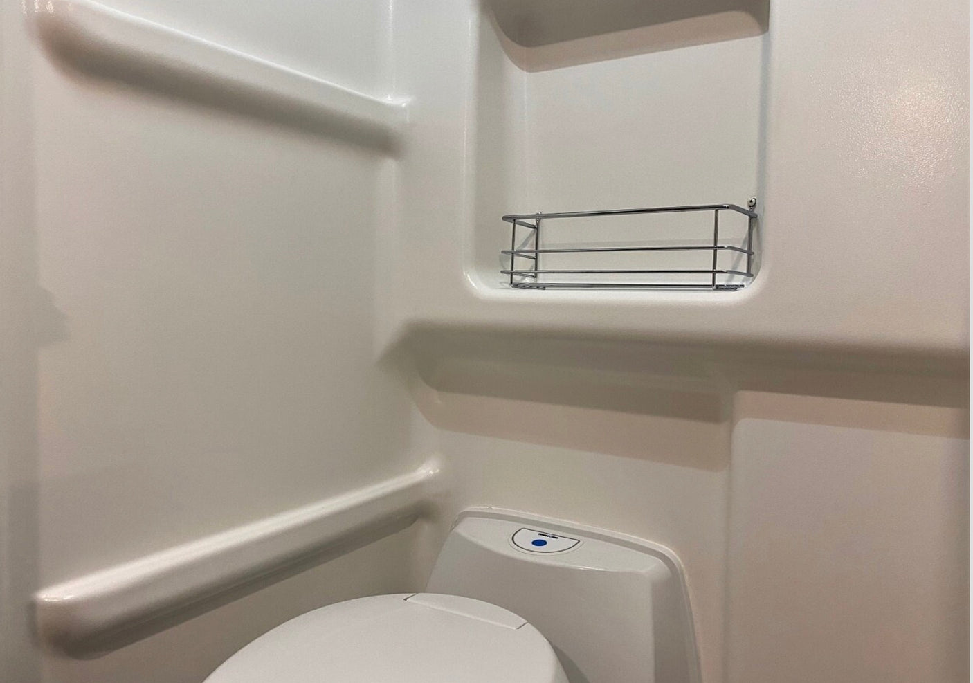 Compact white RV rental bathroom with toilet and a wall-mounted metal caddy, designed for efficient space.