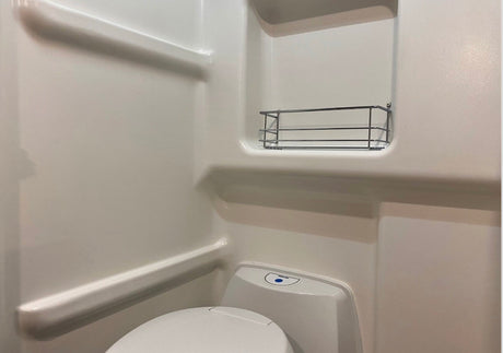 Compact white RV rental bathroom with toilet and a wall-mounted metal caddy, designed for efficient space.