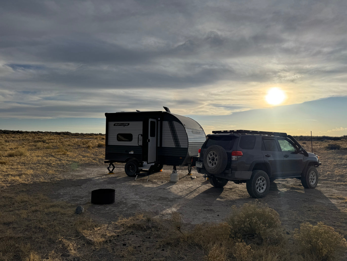 A compact travel trailer, an RV rental, and an SUV are parked on a dry plain, ready for off-grid camping at sunset.