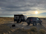 A compact travel trailer, an RV rental, and an SUV are parked on a dry plain, ready for off-grid camping at sunset.