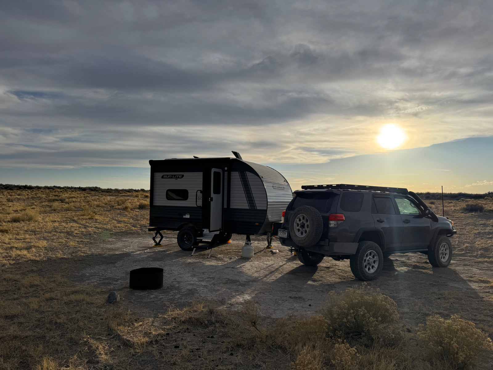 A compact travel trailer, an RV rental, and an SUV are parked on a dry plain, ready for off-grid camping at sunset.