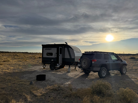 A compact travel trailer, an RV rental, and an SUV are parked on a dry plain, ready for off-grid camping at sunset.