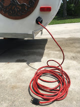Hooking up an RV rental: Red extension cord provides shore power to a white camper on a sunny driveway.