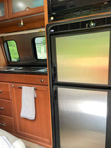 RV rental kitchen view: features stainless fridge, microwave, sink, and wooden cabinets. Windows show outside.