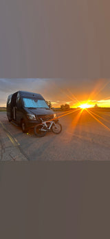 Sunset illuminates an RV rental van & road bike. Ideal for cycling trips & van life adventures.