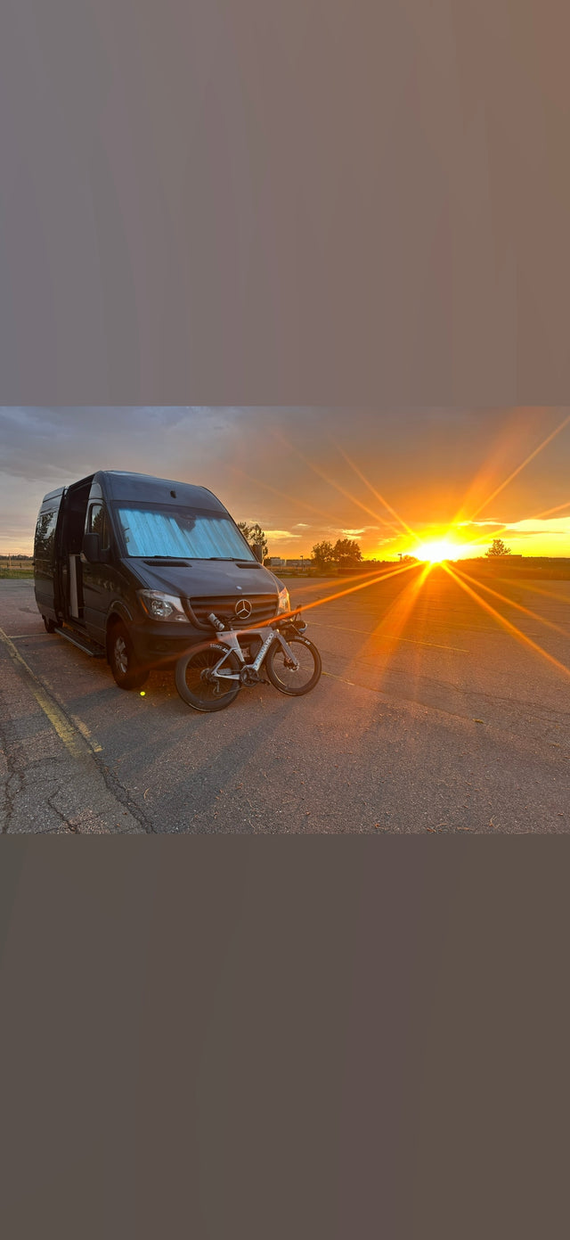 Sunset illuminates an RV rental van & road bike. Ideal for cycling trips & van life adventures.