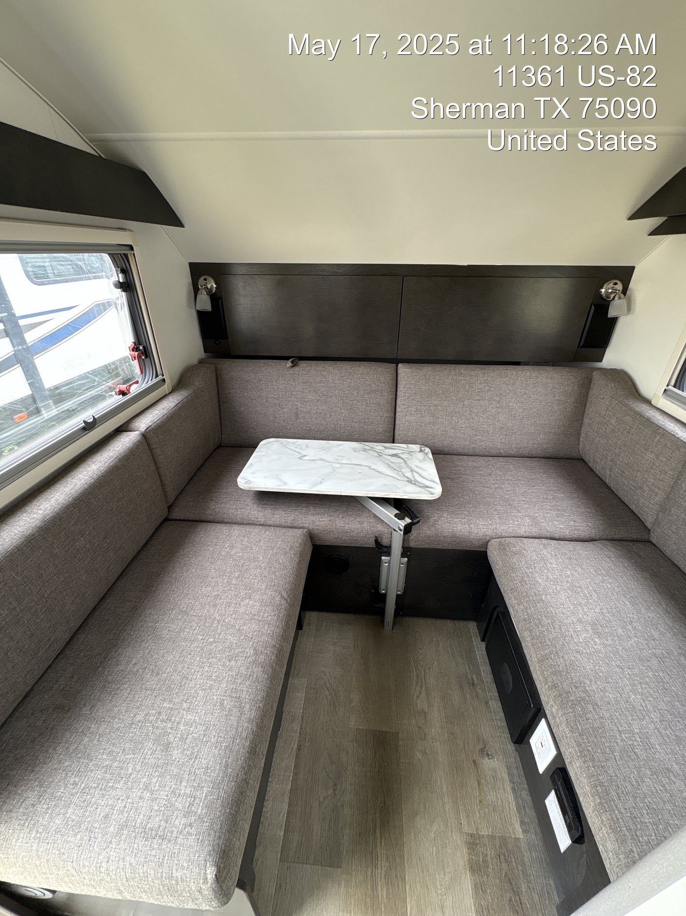 Inside an RV rental, a cozy gray U-shaped dinette and adjustable marble-pattern table on wood-style flooring, Sherman, TX.