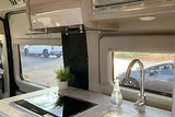 RV rental interior showing a compact kitchen with induction cooktop, sink, and a view of parked vehicles outside.