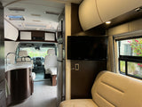 Modern rv rental interior with kitchen, living area, TV, and driver's cabin visible, offering comfort and style.