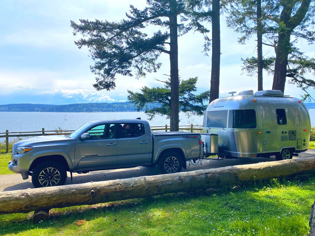 Enjoy serene waterside camping: A silver truck tows an Airstream travel trailer, perfect for an rv rental escape.