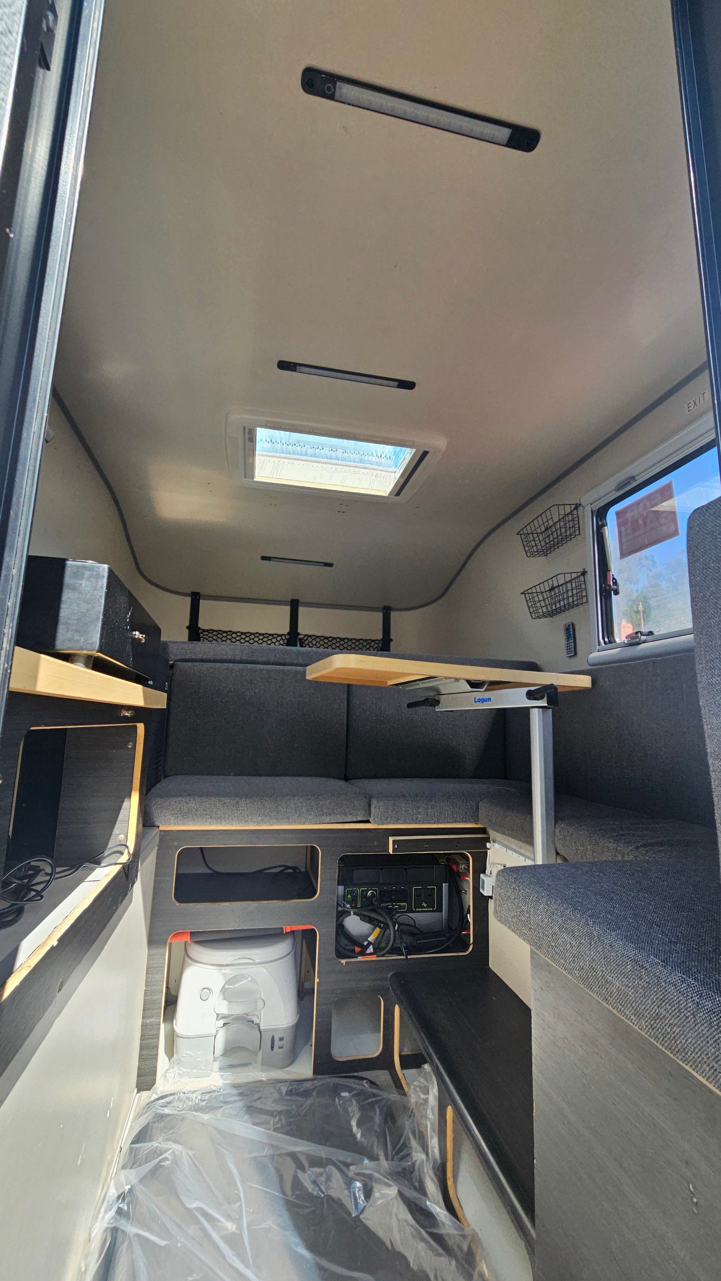 Inside a modern RV rental: comfortable seating with a table, skylight, portable toilet, and power station for off-grid living.