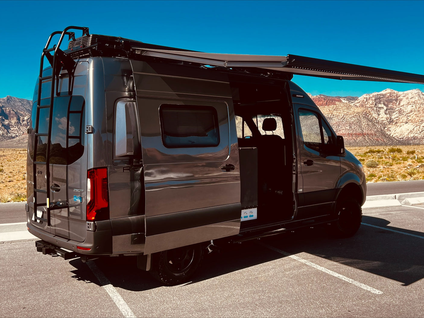 Sleek RV rental van with awning extended, parked in a stunning desert mountain landscape, ready for adventure.