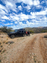 Four friends pose with their black Jeep Wrangler & rooftop tent on a dusty trail, perfect for RV rental adventures.