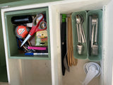 This RV rental cabinet features organized tools like a tape measure and scissors, alongside kitchen utensils and measuring cups.