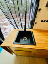 RV rental van interior features a bamboo counter, black sink with faucet, and mesh screen overlooking a snowy outdoor view.