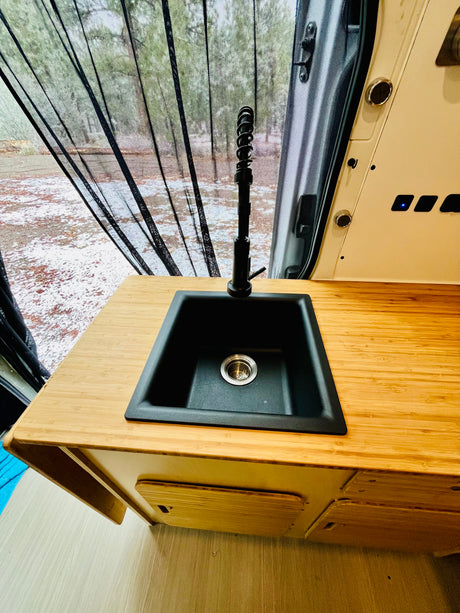 RV rental van interior features a bamboo counter, black sink with faucet, and mesh screen overlooking a snowy outdoor view.
