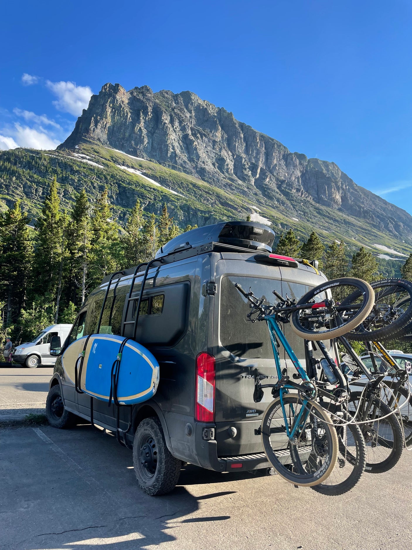 Adventure-ready RV rental van with bikes, paddleboard, and roof box before a majestic mountain.