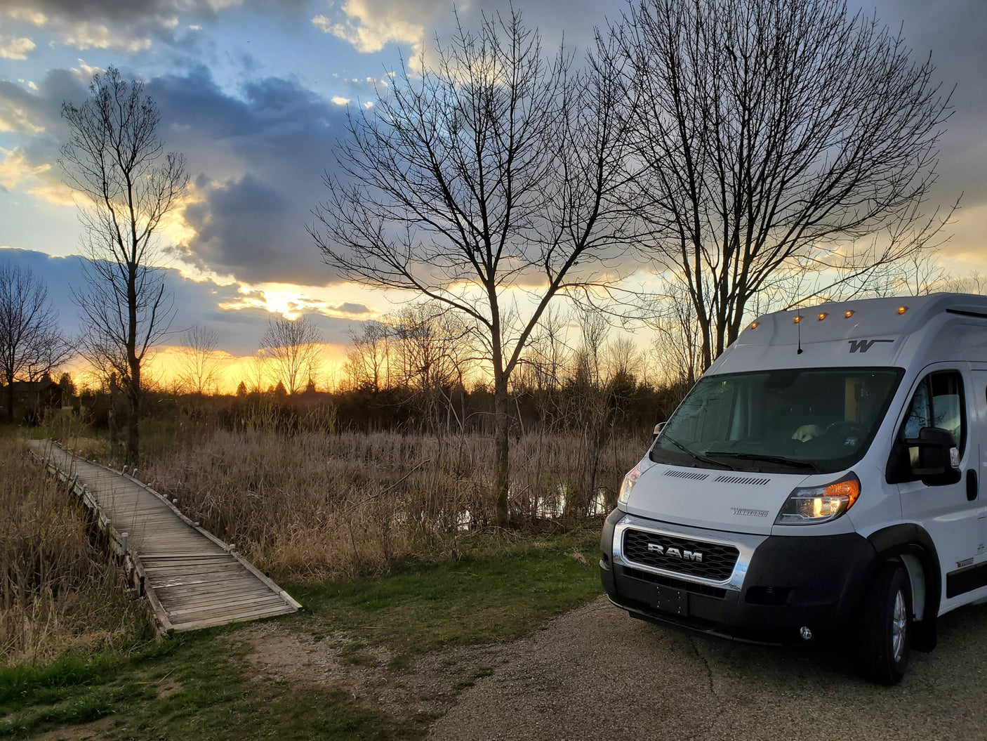 An RV rental parked at sunset beside a rustic wooden boardwalk and marshland, showcasing outdoor travel.