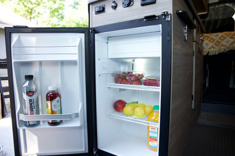 An open RV rental fridge, neatly packed with fresh fruit, kombucha, and juice. Ready for your next adventure!