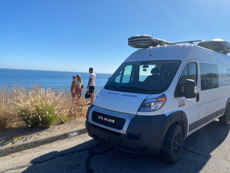 White RAM RV rental parked on a coastal cliff. People and dog gaze at the blue ocean, enjoying the view. — photo 8