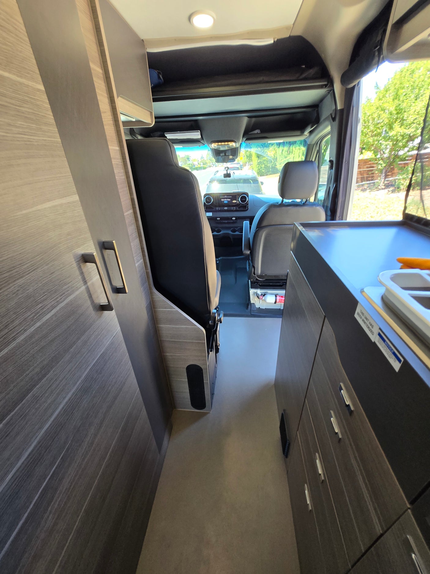 Interior view of an RV rental: a modern camper van showing the cockpit, kitchen counter, and wood-grained storage cabinets.