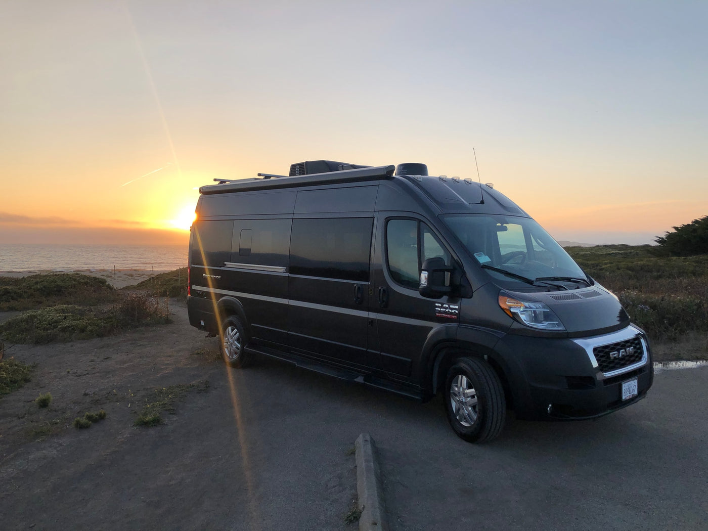 Golden hour RV rental adventure: dark gray camper van overlooking a vibrant ocean sunset by coastal land. — photo 3