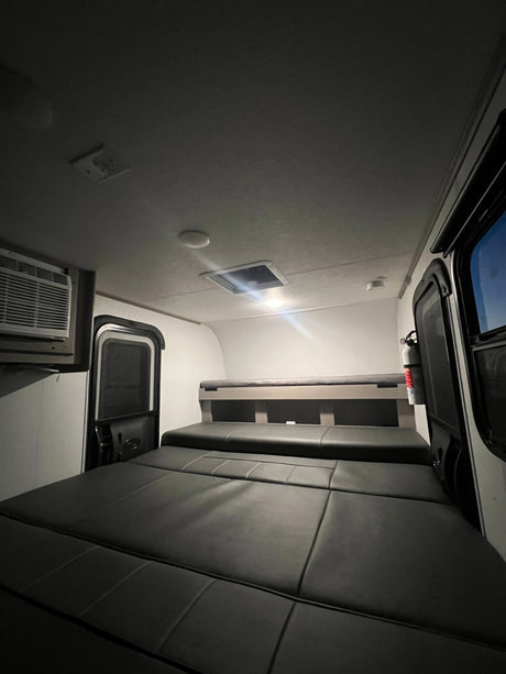 Inside an RV rental: a cozy sleeping area with convertible seating, a top bunk, AC unit, and fire extinguisher, ready for your trip.