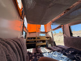 Inside a pop-up rv rental, showing the bed, built-in storage, and desert landscape views from within.