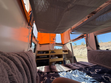 Inside a pop-up rv rental, showing the bed, built-in storage, and desert landscape views from within.