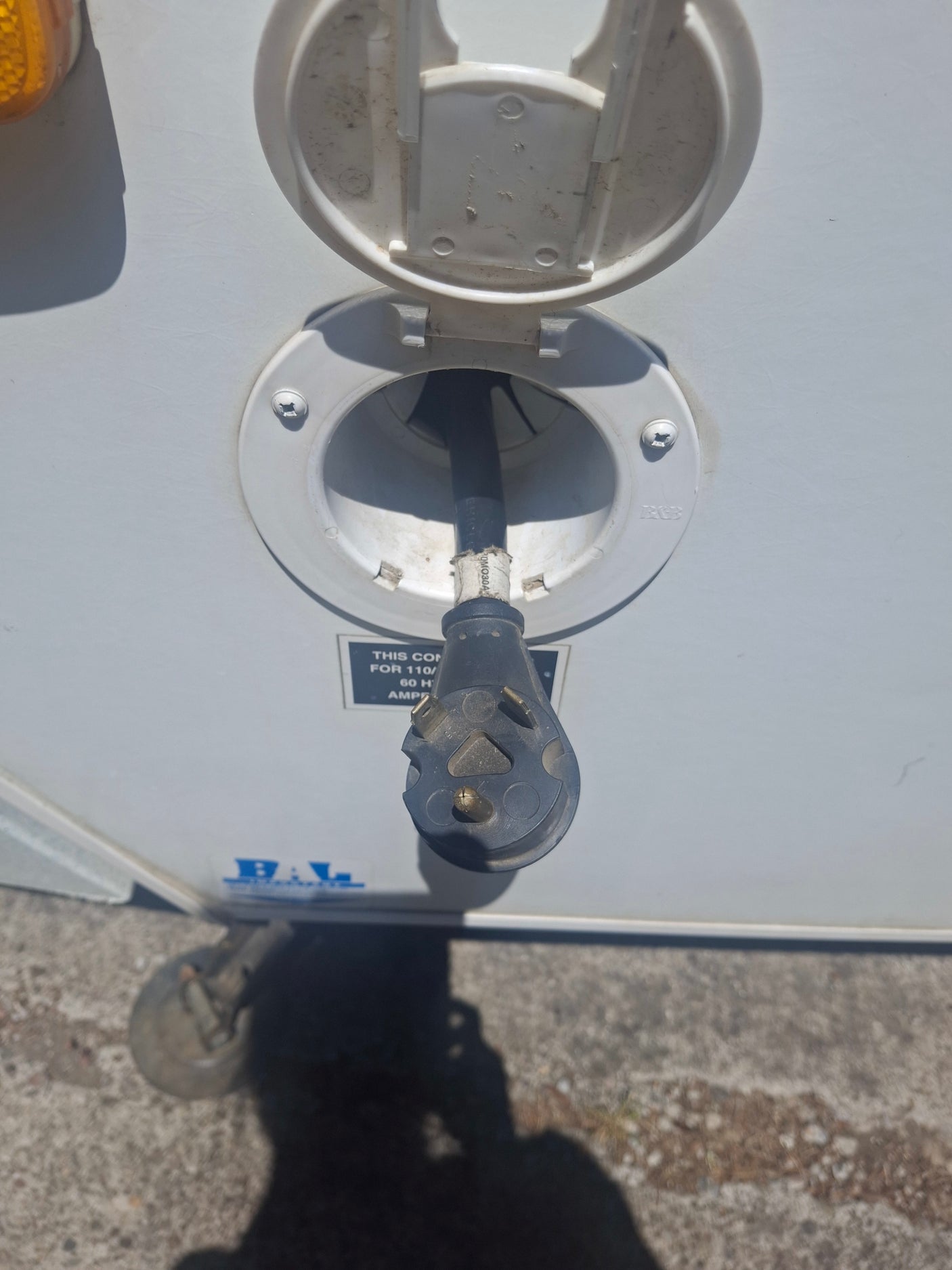 RV rental setup: A 30-amp shore power cord is plugged into the white electrical inlet on an RV.