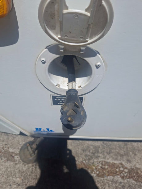 RV rental setup: A 30-amp shore power cord is plugged into the white electrical inlet on an RV.