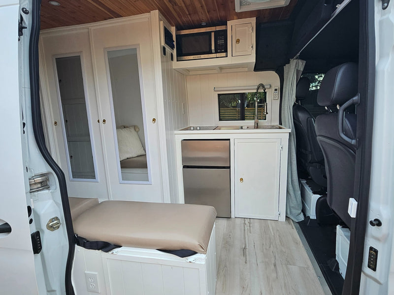  parked. Features small windows & roof cameras. Overcast sky.|This RV rental offers a well-appointed camper van interior with twin bench seating — photo 3