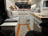 Inside a comfy rv rental, featuring a bed with patterned quilt, compact kitchen, and a plush seating area with storage.
