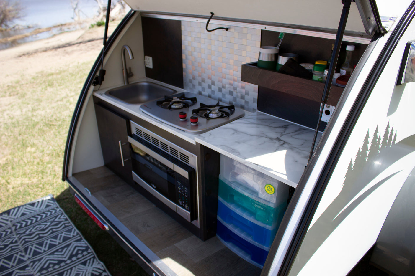 This RV rental's compact outdoor kitchen features a sink, two-burner stove, and microwave, perfect for camping adventures.