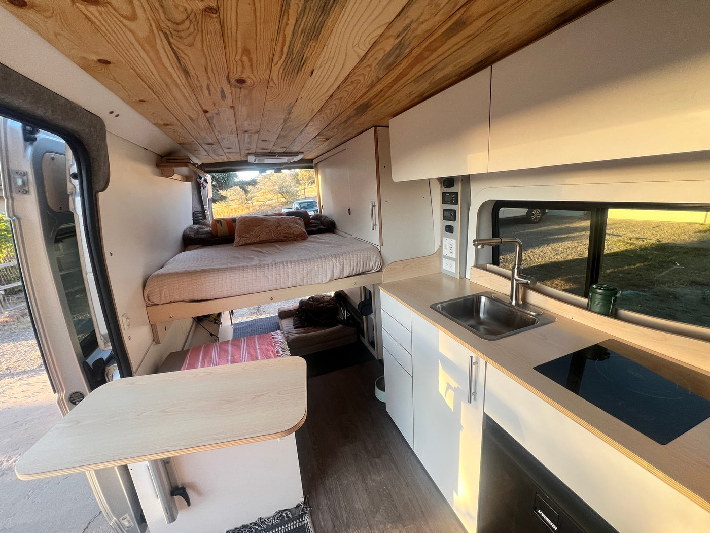 Inside a custom RV rental camper van, featuring an elevated bed, full kitchenette, and dining table. — photo 4