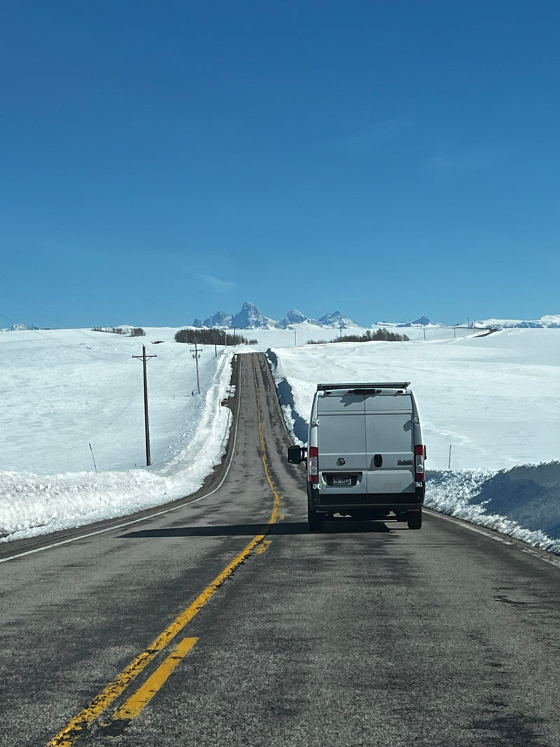White RV rental van on a snowy road with distant Teton Mountains under a clear blue sky. — photo 2