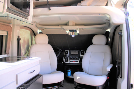 RV rental interior: Front cabin with white captain's chairs, dashboard, and integrated kitchen with microwave.