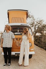 A joyful couple holds hands by their classic orange VW Westfalia camper, ideal for an RV rental road trip.
